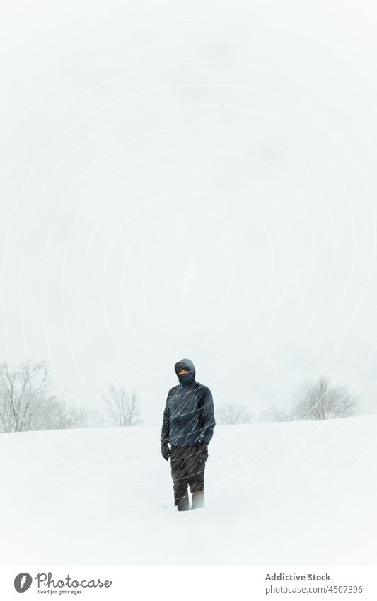 Man in outerwear standing in snowy winter nature man snowfall blizzard cold haze overcast environment male wintertime warm clothes valley leafless trunk