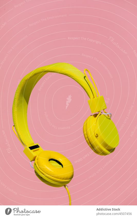 Yellow headphones on pink background modern music listen wireless colorful bright sound device audio vibrant song vivid hang levitate entertain tune gadget red