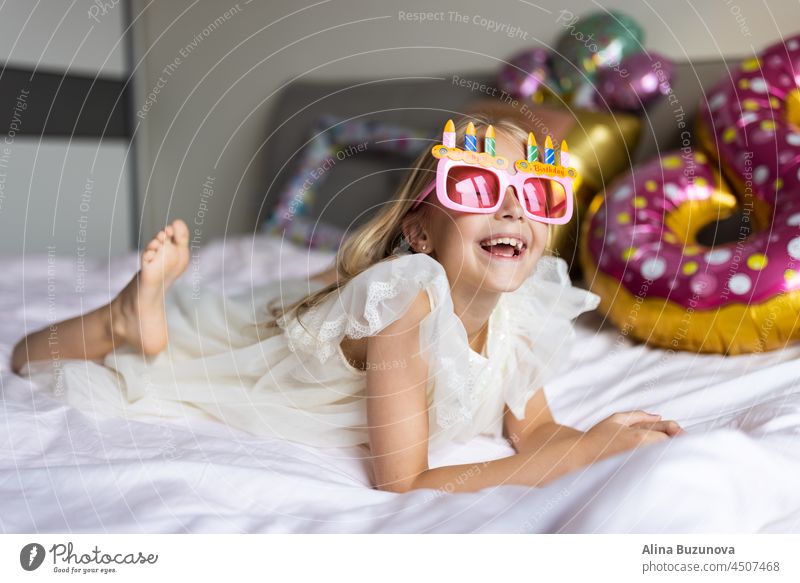 Cite little caucasian girl celebrating eight years old birthday at home. Stylish Kid wearing fashionable dress and having fun with confetti on bed Confetti
