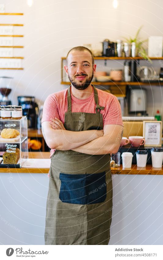 Cheerful barista standing near counter man coffee house work service staff workplace appliance profession supply professional apron male job employee occupation