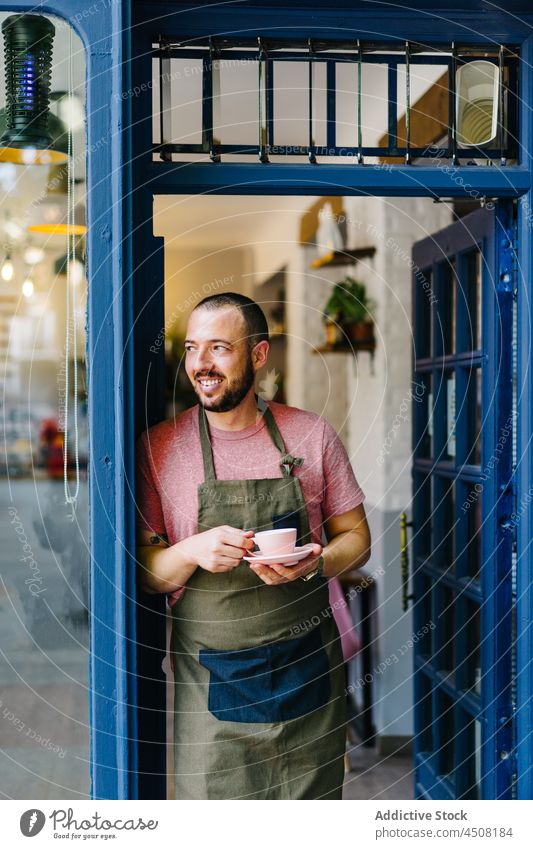 Cheerful barista with coffee standing in doorway man coffee house cup work entrance hot drink beverage staff professional cafeteria apron male job employee