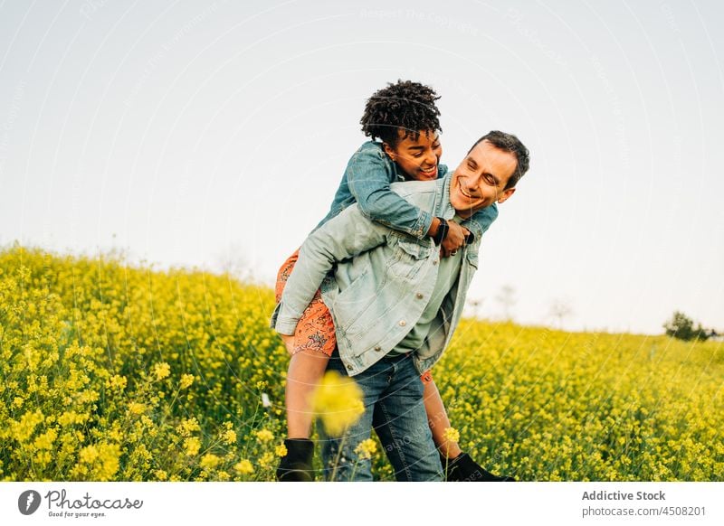Loving man giving piggyback ride to ethnic girlfriend in nature couple smile cuddle love romantic relationship together meadow countryside field happy affection