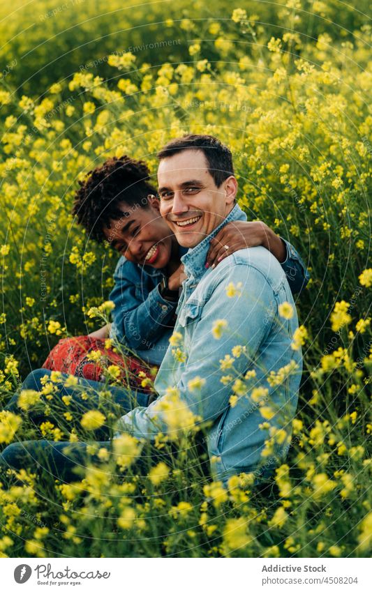 Happy young diverse couple looking at camera in meadow in sunlight date romantic love together relationship affection nature multiracial multiethnic