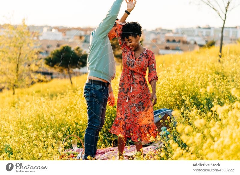 Romantic multiethnic couple dancing in meadow in sunlight dance romantic date picnic together love relationship holding hands spin around affection boyfriend