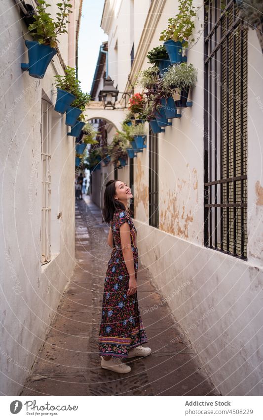 Positive Asian woman in narrow street with potted plants passage building flower flowerpot decor town tourist house residential observe admire flora floral