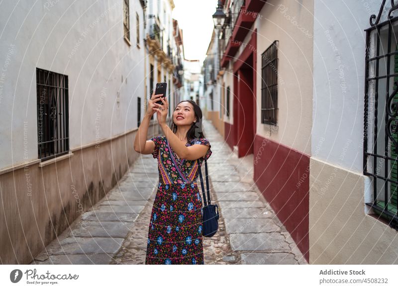 Cheerful Asian woman taking photo on narrow street smartphone take photo photography capture town building tourist aged observe admire moment memory house