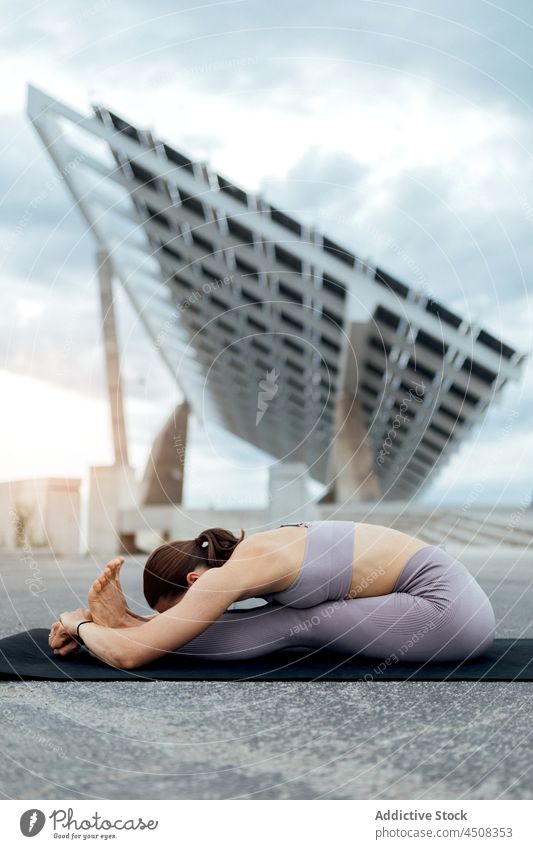 Woman doing seated forward fold asana on street woman yoga solar panel exercise training practice energy female flexible lady workout modern balance sportswear