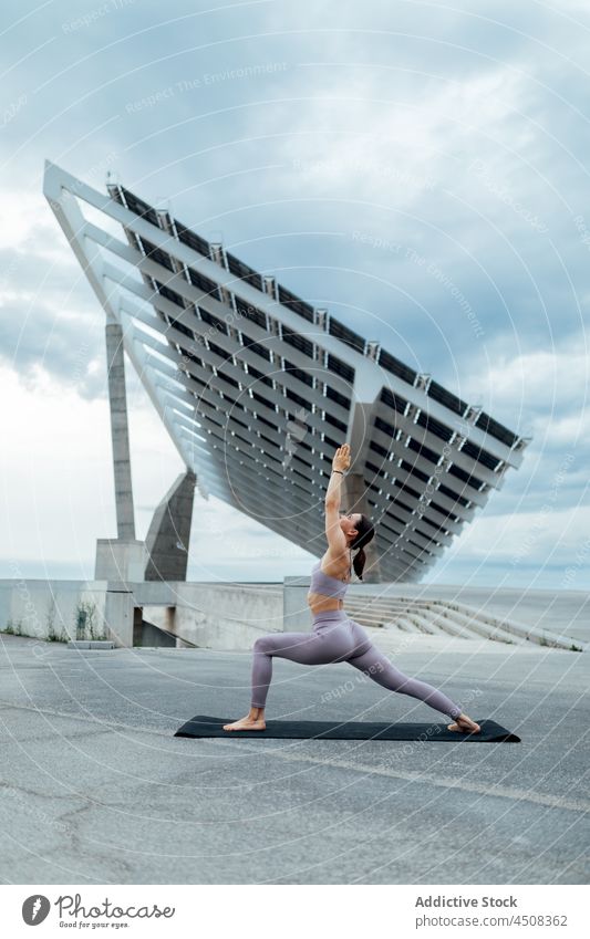 Woman doing warrior asana on street woman yoga solar panel exercise training practice energy female flexible lady workout modern balance sportswear wellness