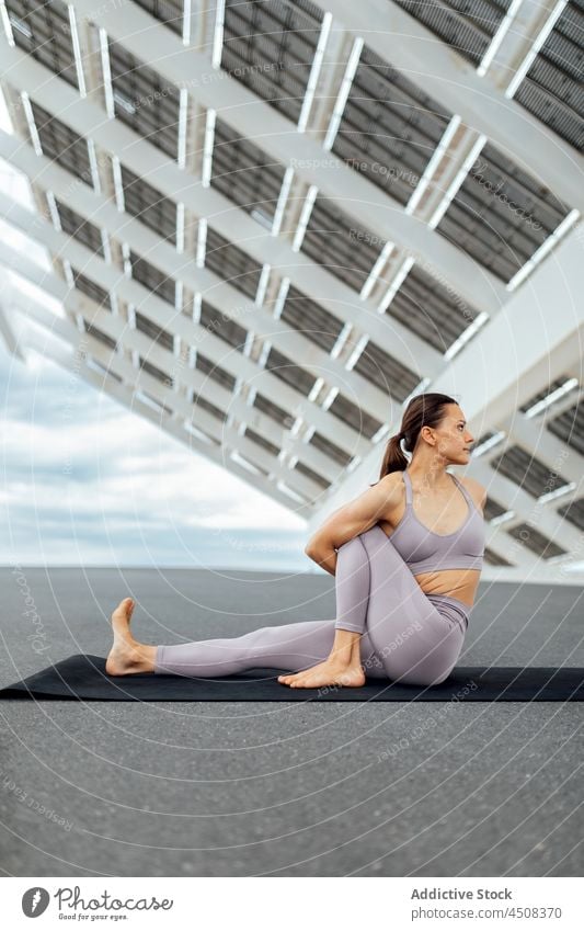 Woman doing revolved sage marichis asana on street woman yoga solar panel exercise training practice energy female flexible lady workout modern sportswear