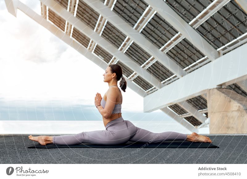 Flexible woman doing Hanumanasana posture yoga hanumanasana front splits forward bend solar panel exercise training street practice energy female flexible lady