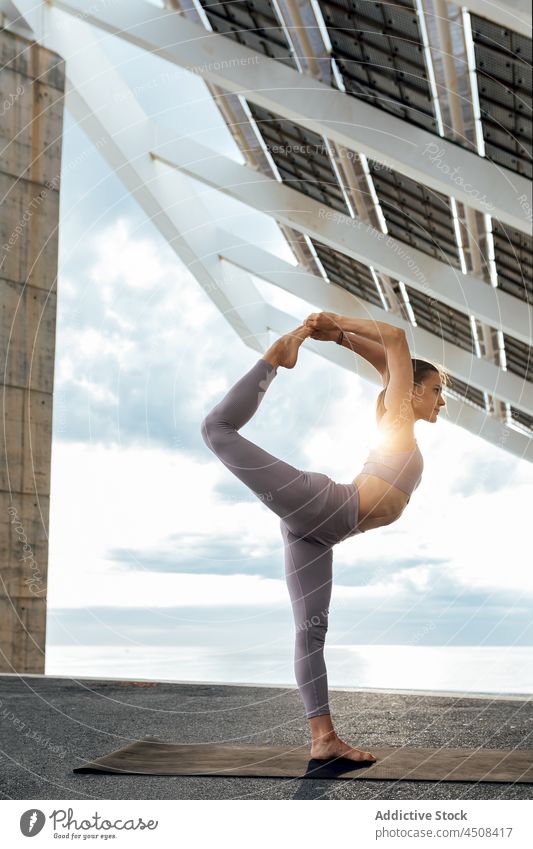 Flexible woman practicing yoga asana near solar panel standing split bent knee exercise training street practice energy female flexible lady workout balance