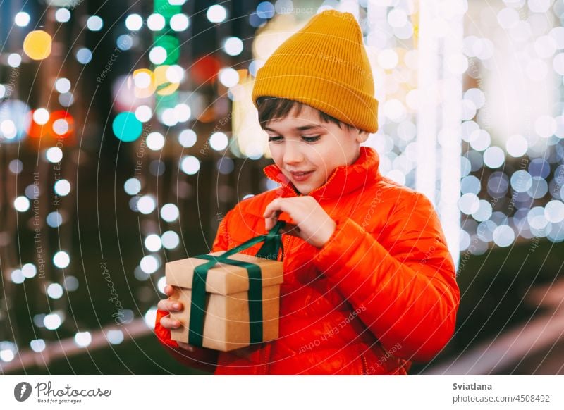 Portrait of a happy boy standing on the evening street and opening a Christmas gift. Christmas gifts, holiday atmosphere. The concept of Christmas and New Year