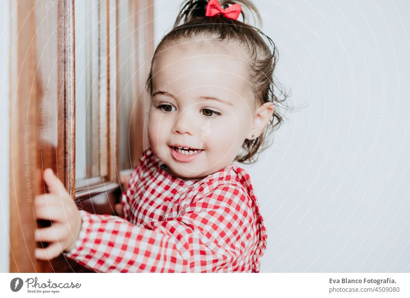 close up portrait of beautiful baby girl at home looking by window door. One year old girl. Lifestyles indoor caucasian waiting gorgeous smiling happy innocence