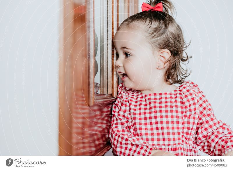 close up portrait of beautiful baby girl at home looking by window door. One year old girl. Lifestyles indoor caucasian waiting gorgeous smiling happy innocence