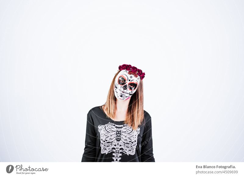 woman wearing mexican face mask during halloween celebration. skeleton costume and red roses diadem on head. woman making silence gesture with finger. Halloween party concept