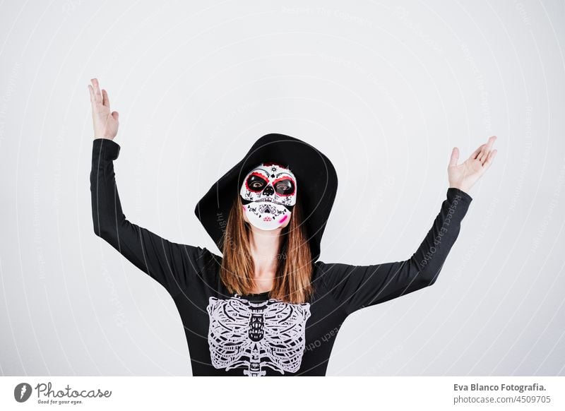 woman wearing mexican face mask during halloween celebration. skeleton costume and black stylish hat. woman with arms raised. Halloween party concept