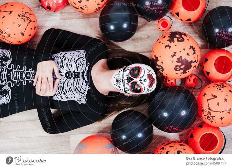 woman wearing mexican face mask during halloween celebration. woman with eyes closed wearing skeleton costume and lying on the floor pretending to be dead. Halloween party concept