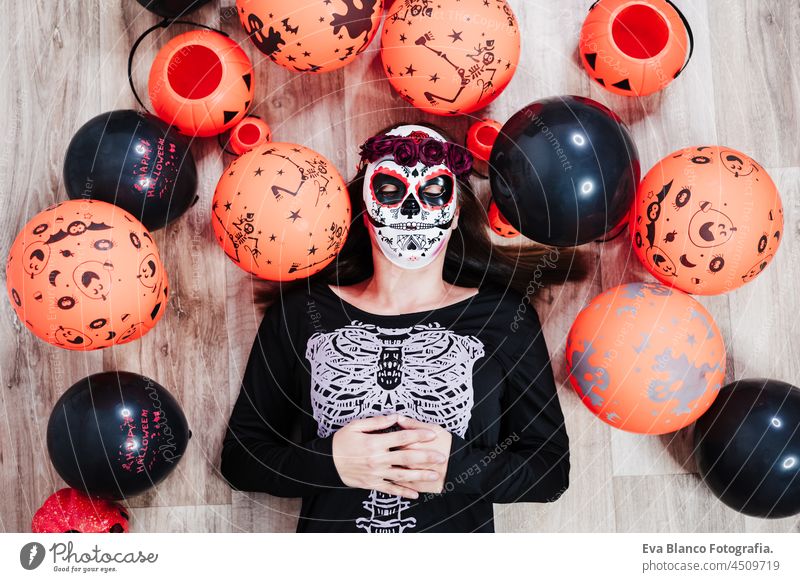 woman wearing mexican face mask during halloween celebration. woman with eyes closed wearing skeleton costume and lying on the floor pretending to be dead. Halloween party concept