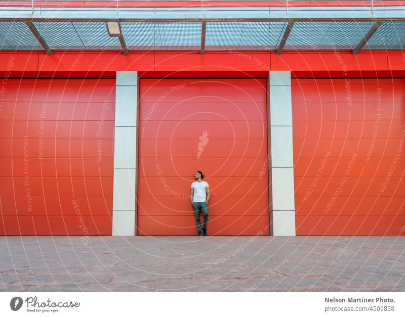 Man portrait leaning on a red warehouse door factory minimal minimalism storage architecture building wall industrial garage front view entrance clean