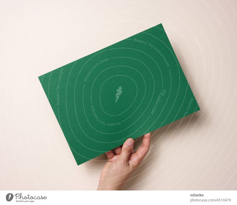Female hand holding empty green paper on a beige background. Copy space ad adult advertise advertisement advertising announcement arm blank business card