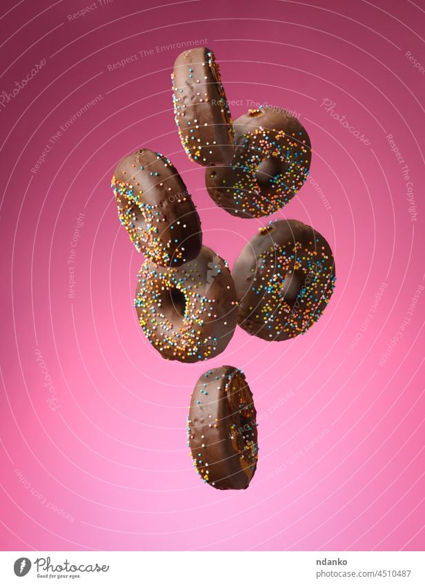 chocolate round donuts with multicolored sugar sprinkles levitate on a pink background doughnut food sweet fly glazed bakery dessert pastry flying calorie baked