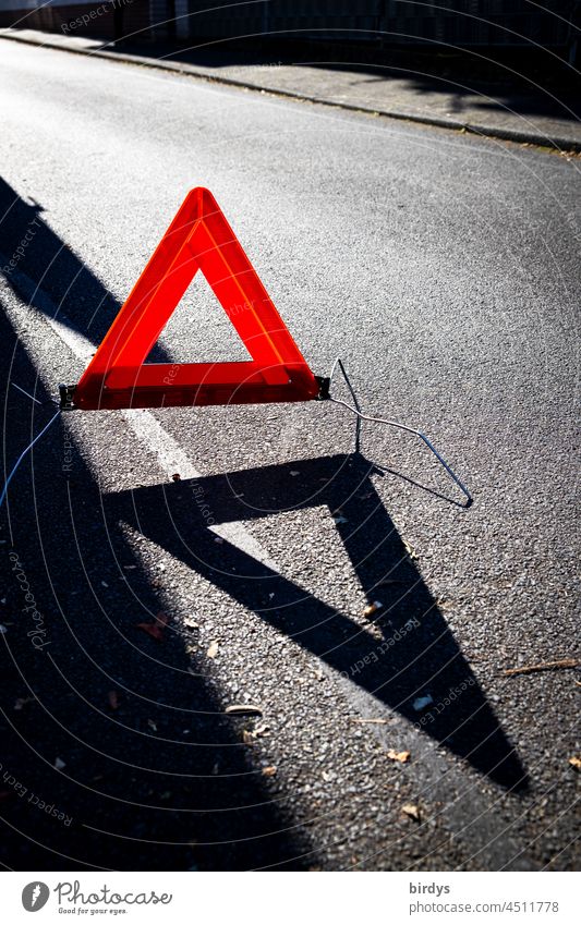 Red warning triangle in backlight with shadow cast on a street danger spot red triangle Shadow Street Asphalt luminescent Gray signal effect peril Breakdown