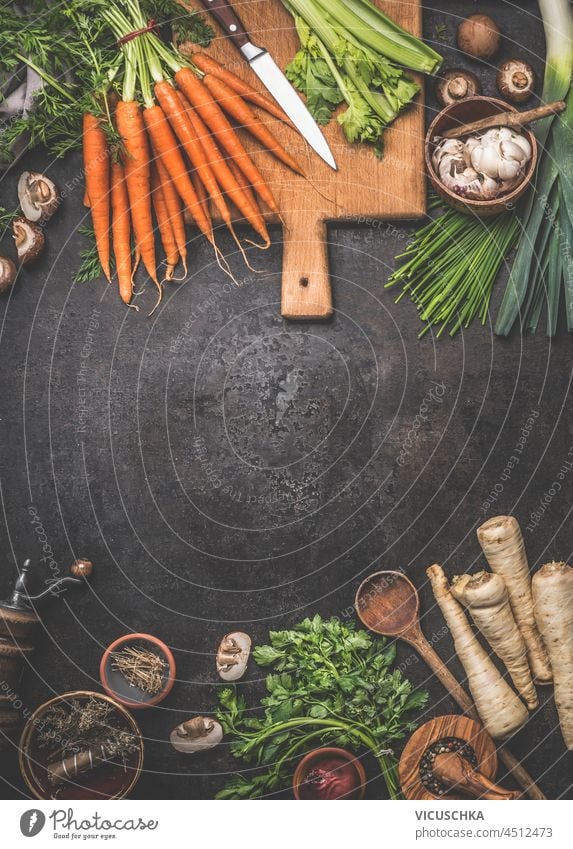 Food background with various vegetables and ingredients: carrot, mushrooms, parsnip, garlic, kitchen utensils on dark concrete table. Cooking with healthy seasonal vegetables. Top view with copy space