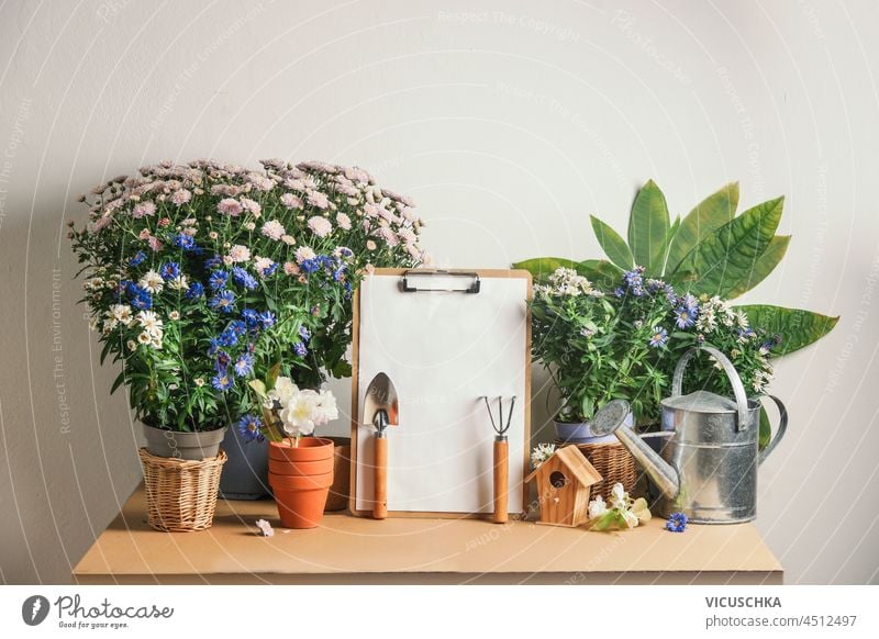 Gardening table with empty to do list, gardening equipment and potted flowers white wall background front view copy space blooming botanical botany bouquet