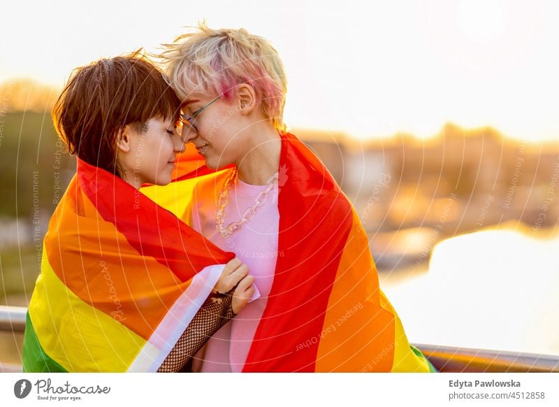 Young non binary couple in love hugging under a rainbow flag homosexual couple together romantic queer non-binary gender fluid lgbt equality millennials
