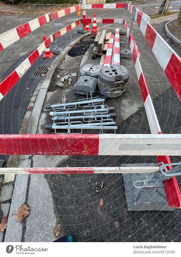 Civil engineering construction site. A small section of a sidewalk is being repaired. It is surrounded by a construction barrier made of planks in red and white. There is construction equipment available as well.