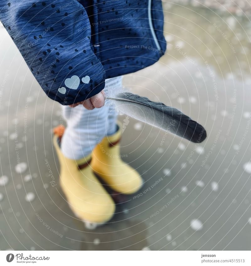 Toddler with yellow rubber boots holds a feather in hand Yellow Rubber boots Feather Puddle Rain Autumnal Infancy Child Childlike Children`s hand out