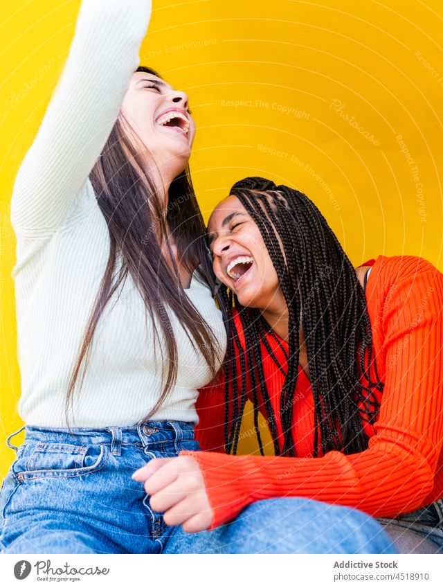 Cheerful multiracial women laughing against yellow background friend happy jeans sweater cheerful friendship style positive female diverse multiethnic casual