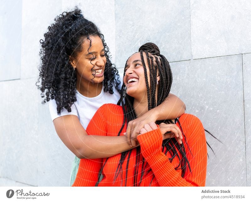 Smiling diverse friends standing and embracing on street women hug embrace happy cheerful urban smile positive female multiracial multiethnic trendy style wall