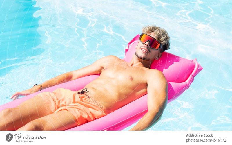 Relaxed man on inflatable mattress rest swimming pool relax sunbath water leisure summer shirtless male suntan sunglasses chill naked torso sunlight