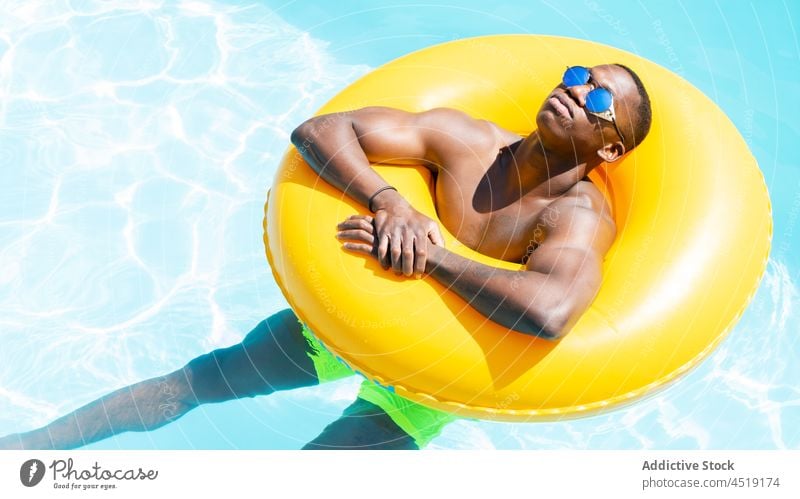Relaxed black man on inflatable ring rest swimming pool relax sunbath water leisure summer shirtless male suntan sunglasses chill yellow naked torso sunlight
