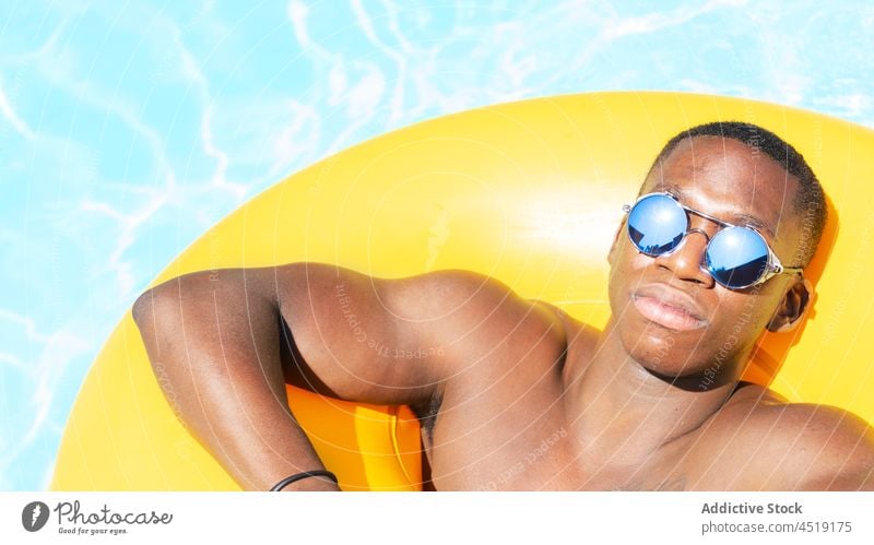 Relaxed black man on inflatable ring rest swimming pool relax sunbath water leisure summer shirtless male suntan sunglasses chill yellow naked torso sunlight