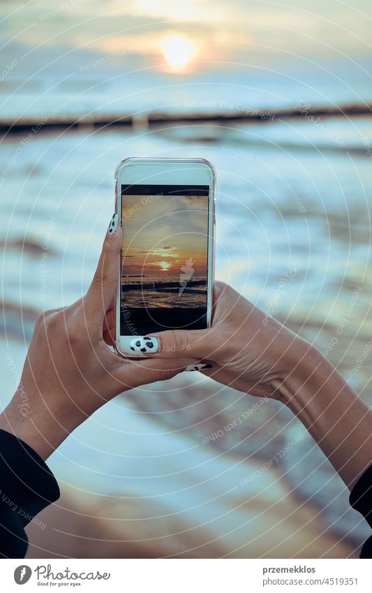 Young woman taking photos of sunset over sea using smartphone during summer trip photographer picture technology screen person female holding ocean photography