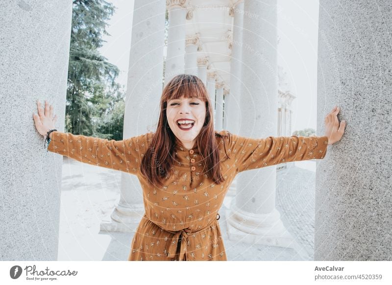 Young hipster woman on an autumnal dress laughs to camera in the middle of an ancient white column construction, hipster happy day, freedom and liberty concepts, ginger woman, social network style