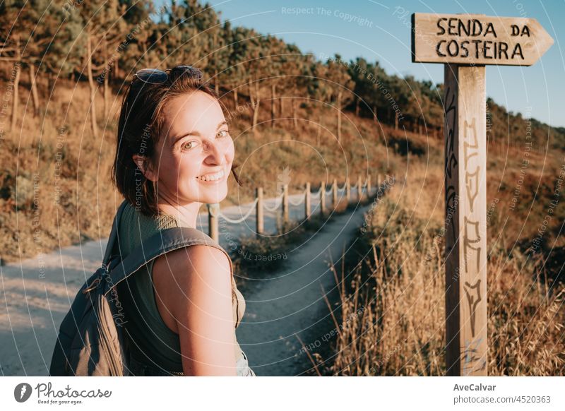 Young hipster girl turning around smiling to camera while doing some hiking on the shore, traveling and low budget travel concepts, copy space woman explore