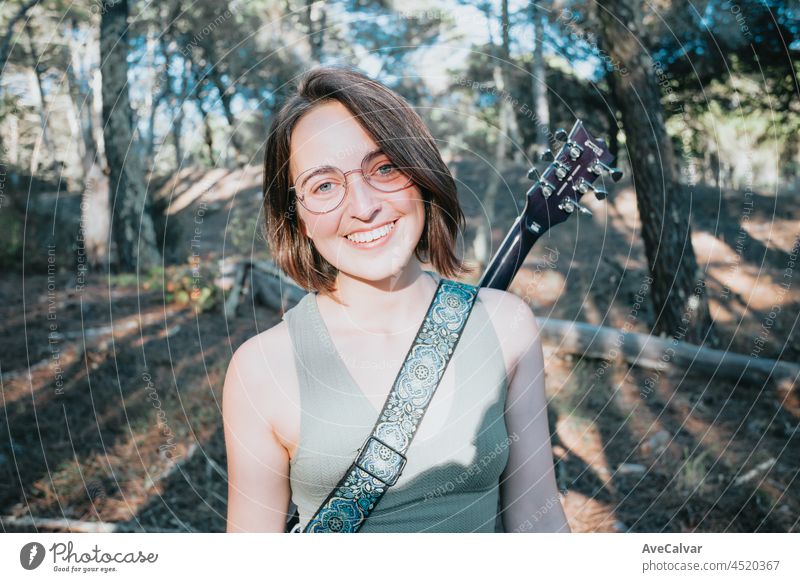 Young hipster girl on glasses smiling to camera with an electric guitar on his back, study music concepts, copy space, social networks, self improvement woman