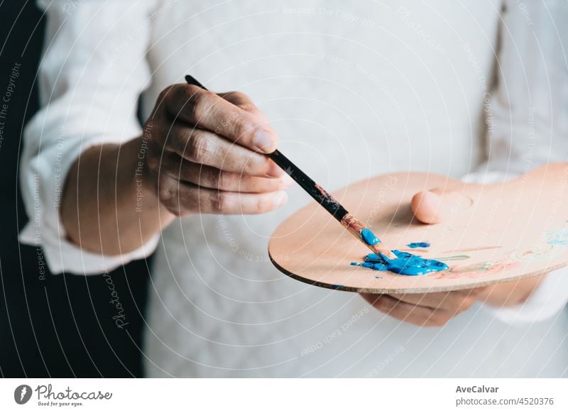 Studio image of an old woman painting a canvas with blue paint. Artist studio concept. Old artist hobby person brush elderly paintbrush painter retirement