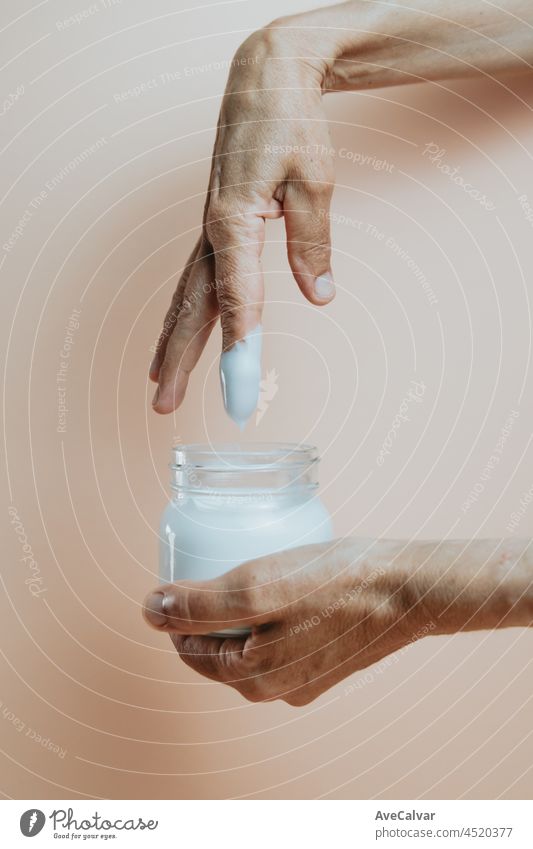 Old hands taking body lotion cream from a bottle, minimalist shot, pastel colour background skin skin care applying skincare routine purity cosmetic female