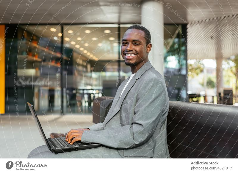 Black businessman typing on laptop on street bench using online work startup project entrepreneur focus netbook device remote browsing busy ethnic