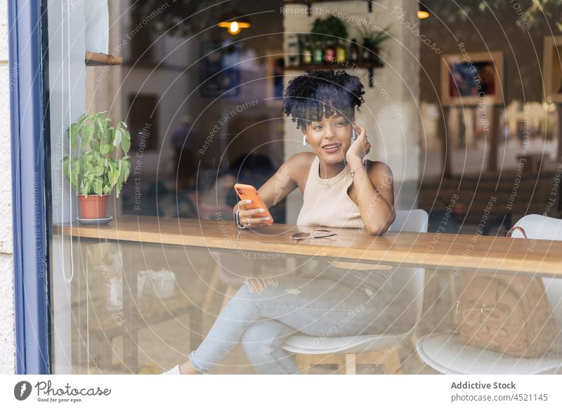 Cheerful black woman during video call via smartphone in cafeteria cheerful communicate conversation talk joy window female young african american ethnic trendy