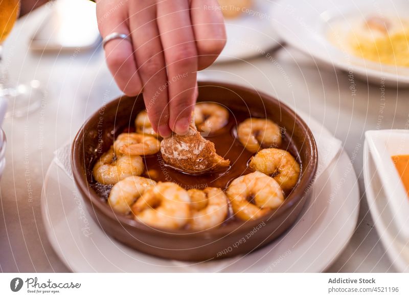 Crop faceless female dipping bread into sauce of shrimp dish woman gambas al ajillo seafood restaurant eat hungry delicious cuisine meal hand tasty appetizing