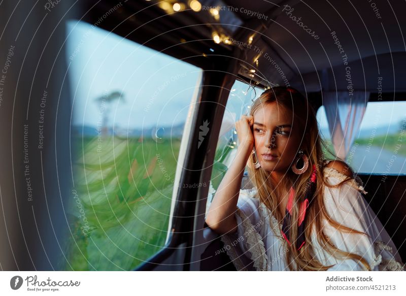 Confident beautiful blonde girl inside a vintage van looking at the camera pretty cute woman caucasian leaning window caravan garland looking away tanned sunset