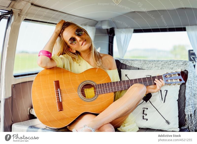 Beautiful blonde girl dressed in summer clothes playing guitar i pretty cute young woman female caucasian music happy leisure sunglasses sitting van caravan