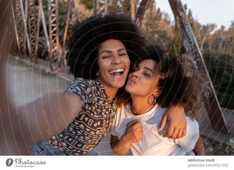 Positive black women hugging and taking selfie best friend pouting lips having fun friendship bonding delight sundown female self portrait kiss memory together