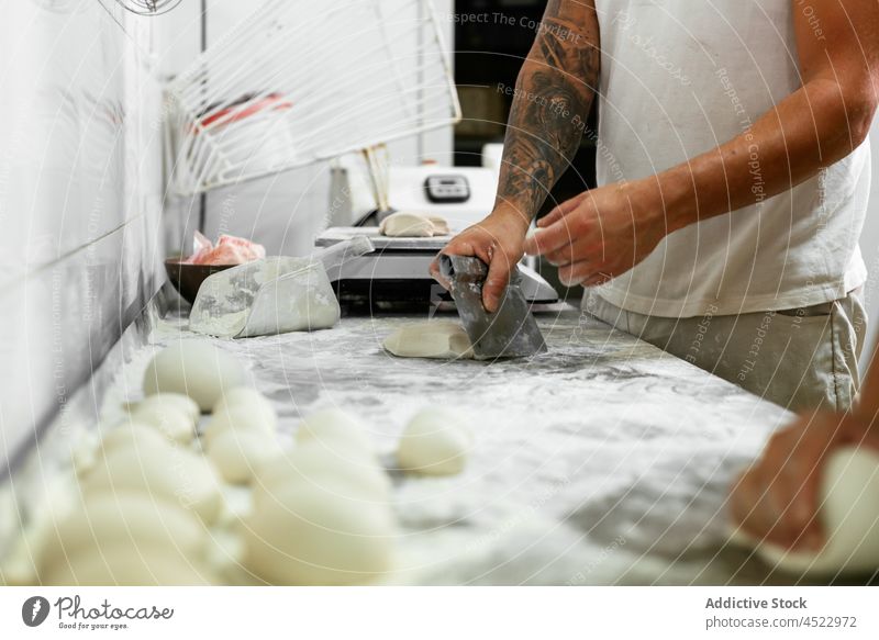 Crop bakers cutting dough in kitchen man bakery work together process flour bread raw piece knead male tattoo casual fresh uncooked pastry job professional