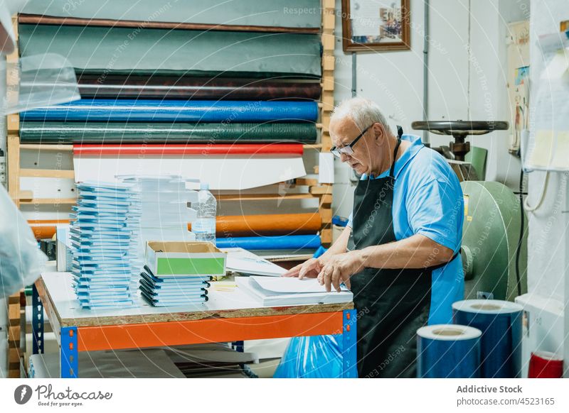 Attentive elderly male worker checking papers in printing studio man artisan attentive workshop concentrate paperwork notebook instrument industry senior